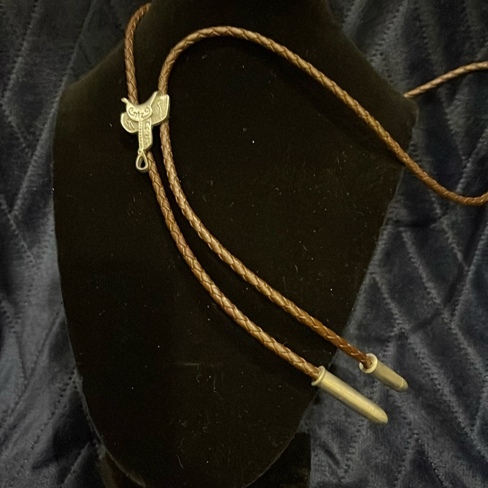Vintage pewter western saddle bolo on brown leather strap. Bullet ends